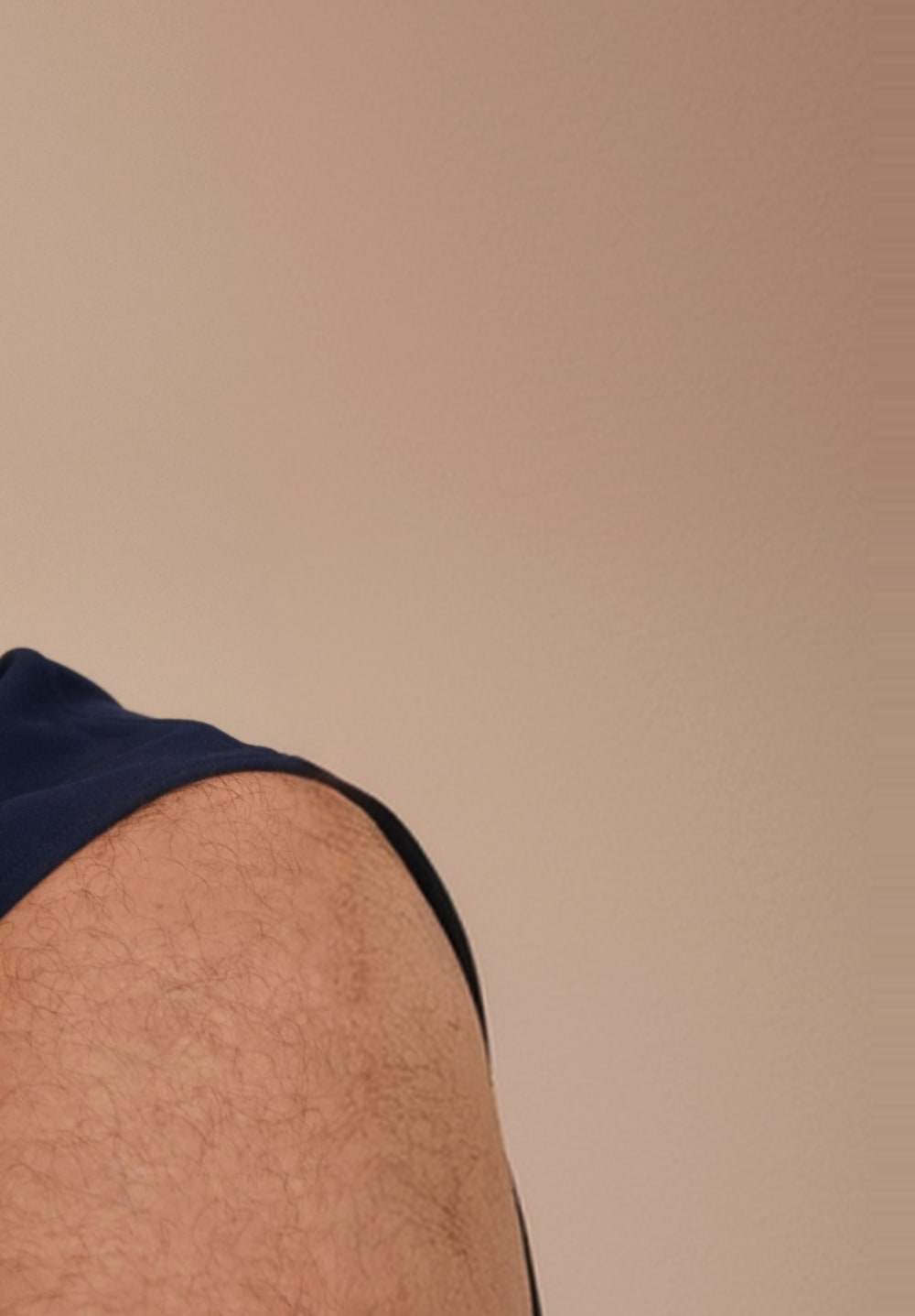 Close-up of a man’s crossed arms against a tan backdrop